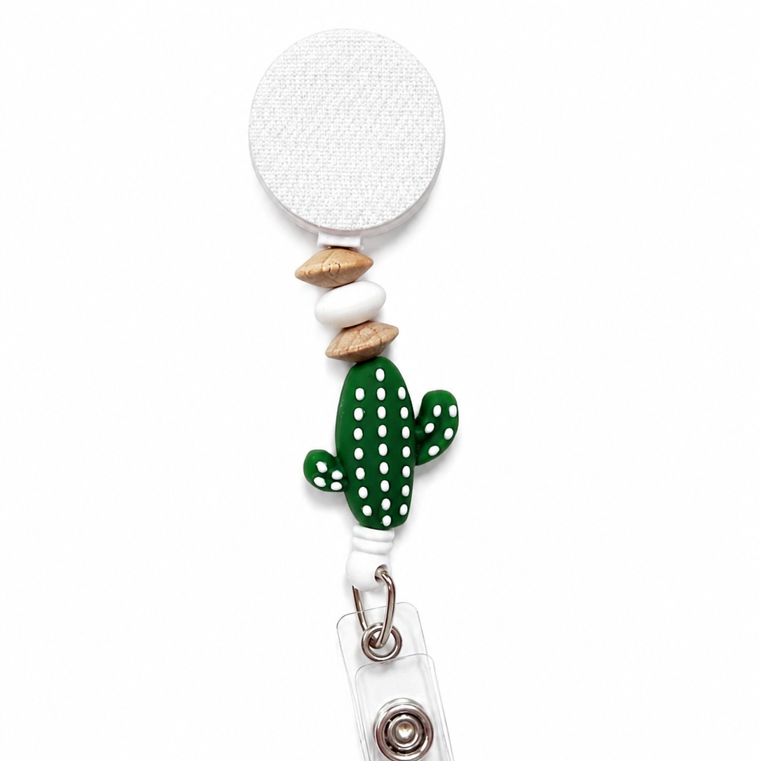 Cactus Oasis badge reel featuring a green cactus focal bead with white dot accents, a white silicone bead, natural wood spacer beads, and a white retractable badge reel.