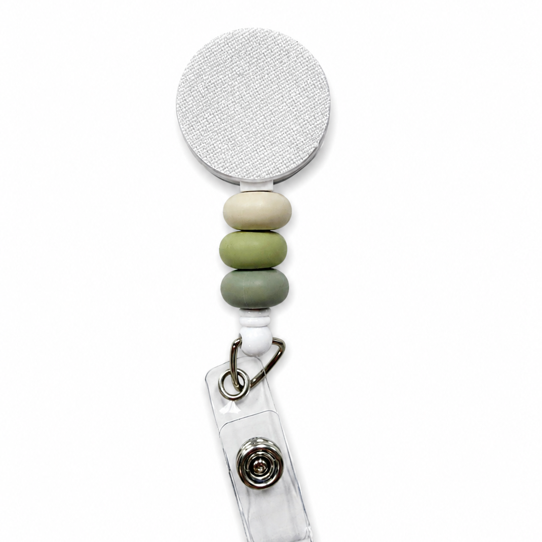 Moss and Stone badge reel featuring cream, sage green, and moss green decorative beads on a white retractable badge reel. Neutral beaded work badge accessory.