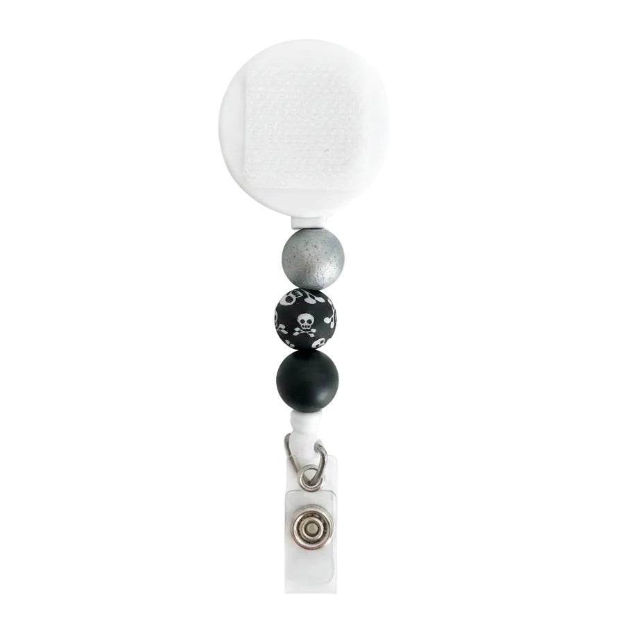 Skull and crossbones beaded badge reel with white retractable reel, metallic silver, black, and skull print silicone beads for a spooky work badge accessory.