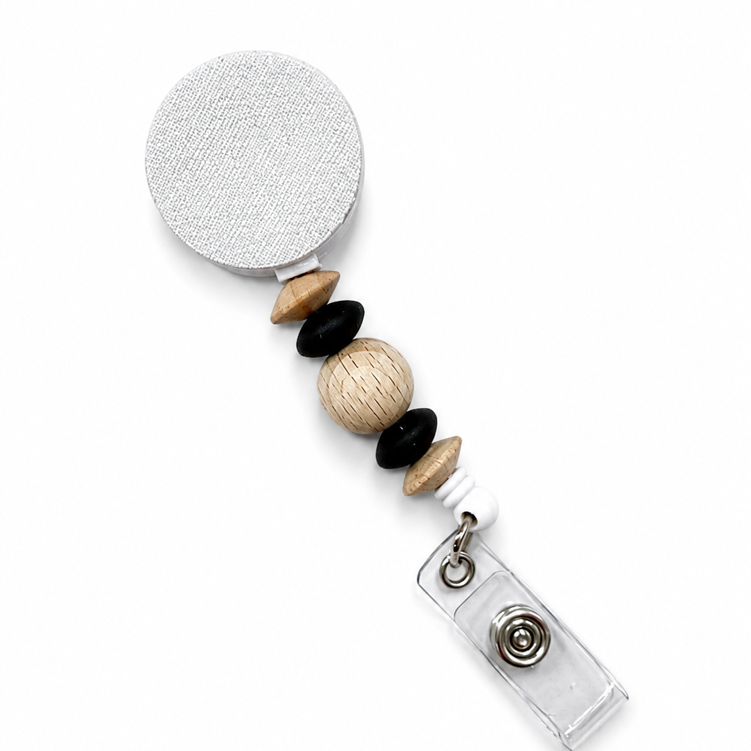 Timber badge reel featuring a natural wood bead, black beads, and wood spacer beads on a white retractable badge reel. Modern beaded work badge accessory.