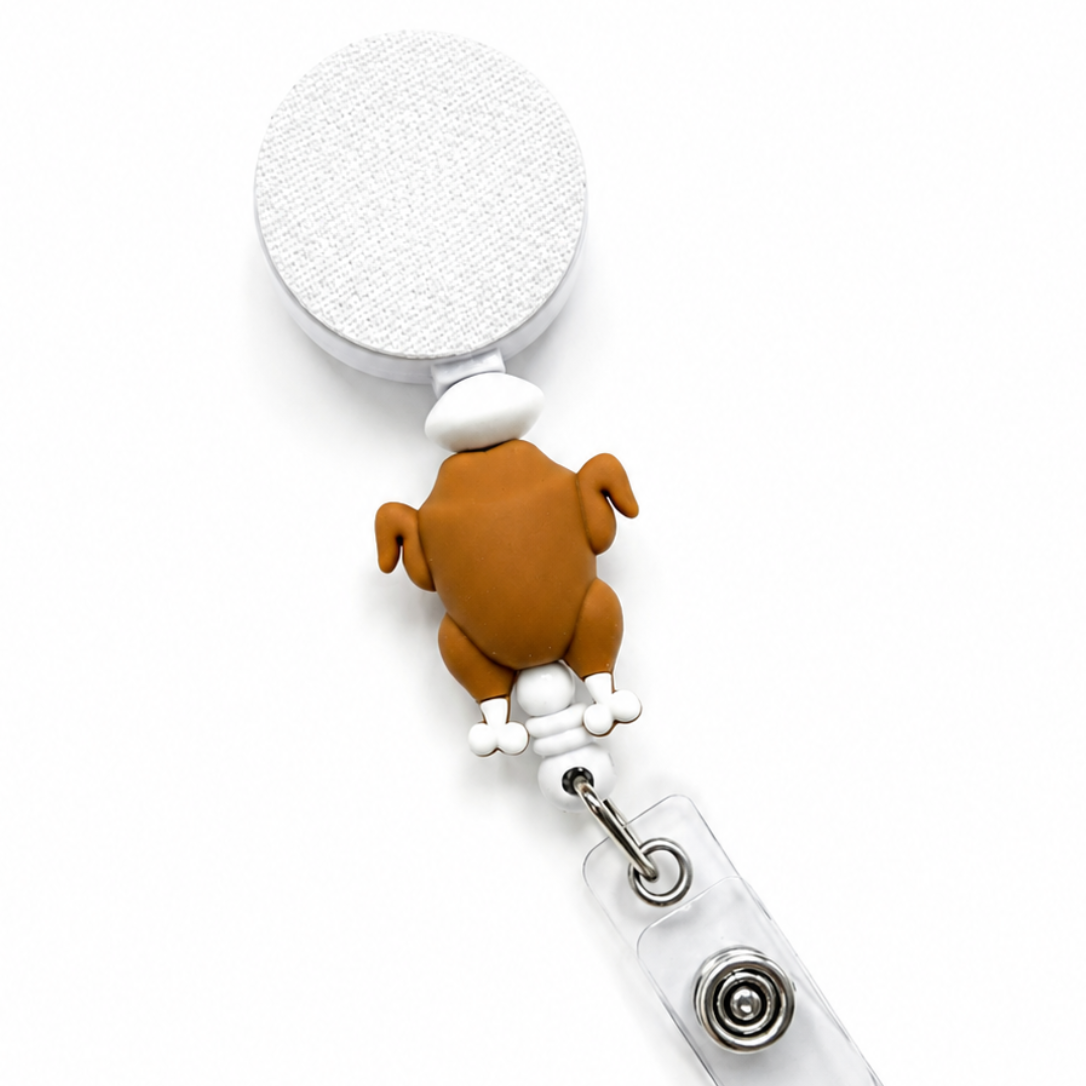 Turkey badge reel featuring a brown turkey design with white decorative accents on a white retractable badge reel. Cute Thanksgiving badge reel and seasonal work badge accessory.
