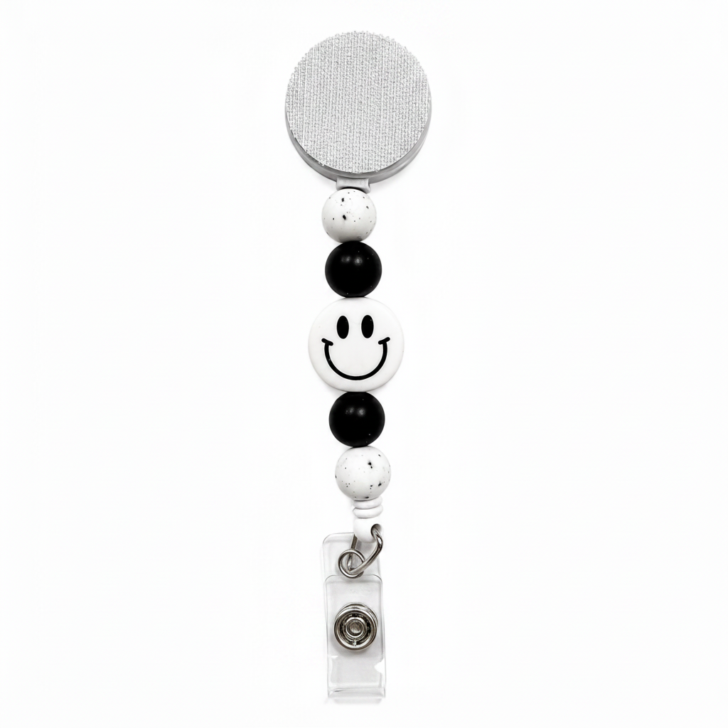 White Smiley Face badge reel featuring a white happy face design with black beads and white speckled decorative beads, retractable badge reel functionality, and secure badge holder attachment.