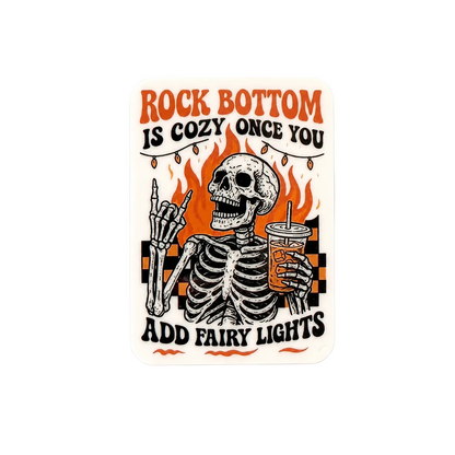 Funny skeleton sticker with “Rock Bottom Is Cozy Once You Add Fairy Lights” quote, retro spooky aesthetic with dark humor design.