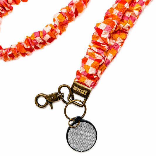 Andi x Katie Lynn Bright Checkered Interchangeable Lanyard featuring vibrant coral, pink, orange, and peach checkered fabric, compatible with interchangeable hardboards and plastic add-ons.