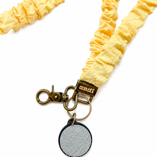 Andi x Katie Lynn Butter Yellow Interchangeable Lanyard featuring a soft butter yellow textured scrunchie-style fabric design, compatible with interchangeable hardboards and plastic add-ons.