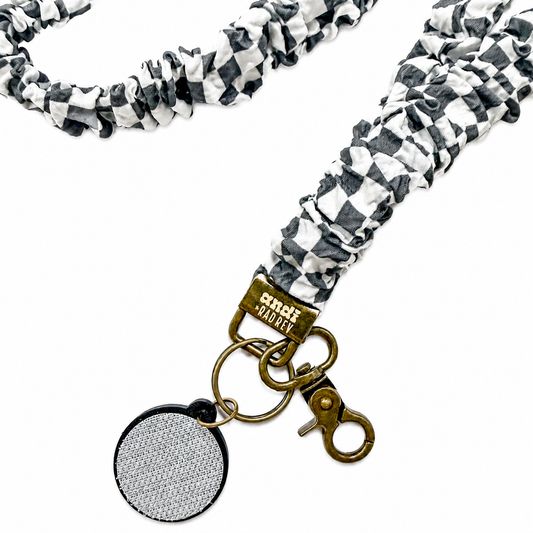 Andi x Rad Rev Grey Checkered Interchangeable Lanyard featuring a gray and white checkered scrunchie-style fabric design, compatible with interchangeable hardboards and plastic add-ons.