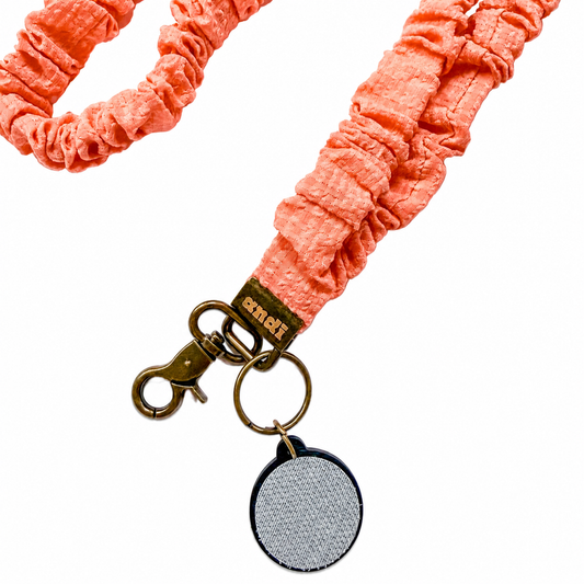 Coral Gingham Interchangeable Andi Lanyard featuring a coral pink textured scrunchie-style fabric design, compatible with interchangeable hardboards and plastic add-ons.