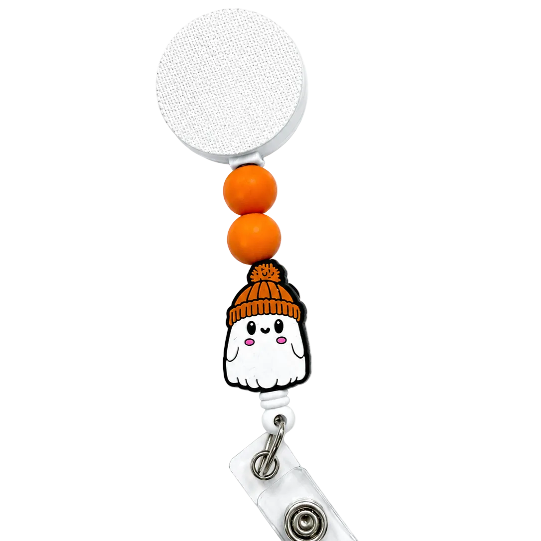 Cozy Ghost badge reel featuring a smiling white ghost wearing an orange knit beanie with orange decorative beads, a retractable badge reel, and secure badge holder attachment.