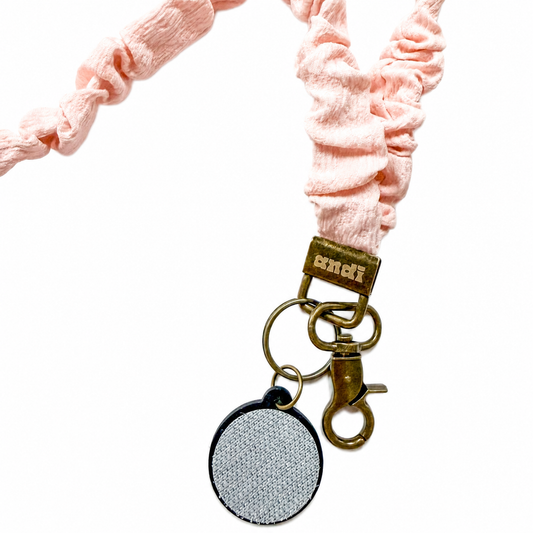 Dainty Pink Interchangeable Andi Lanyard featuring a soft blush pink textured scrunchie-style fabric design, compatible with interchangeable hardboards and plastic add-ons.
