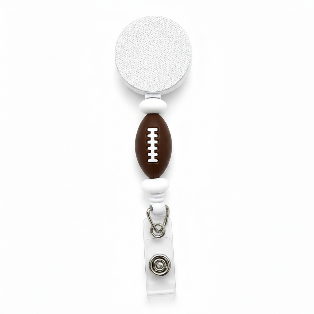 Football badge reel featuring a brown football focal bead with white football laces and white accent beads on a white retractable badge reel. Cute sports-themed work badge accessory.