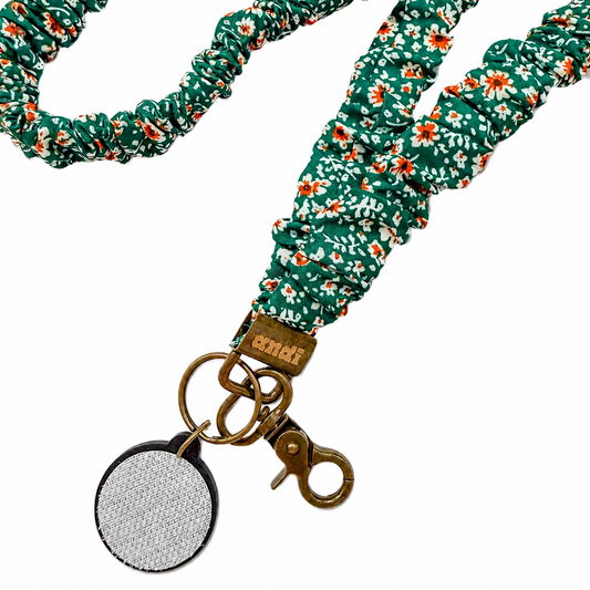 Green Floral Interchangeable Andi Lanyard featuring a teal green floral fabric design with white and orange flowers, compatible with interchangeable hardboards and plastic add-ons.