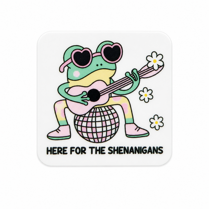 Plastic add-on featuring a frog wearing heart-shaped sunglasses, playing a guitar on a disco ball with the phrase "HERE FOR THE SHENANIGANS," compatible with interchangeable badge reel bases.