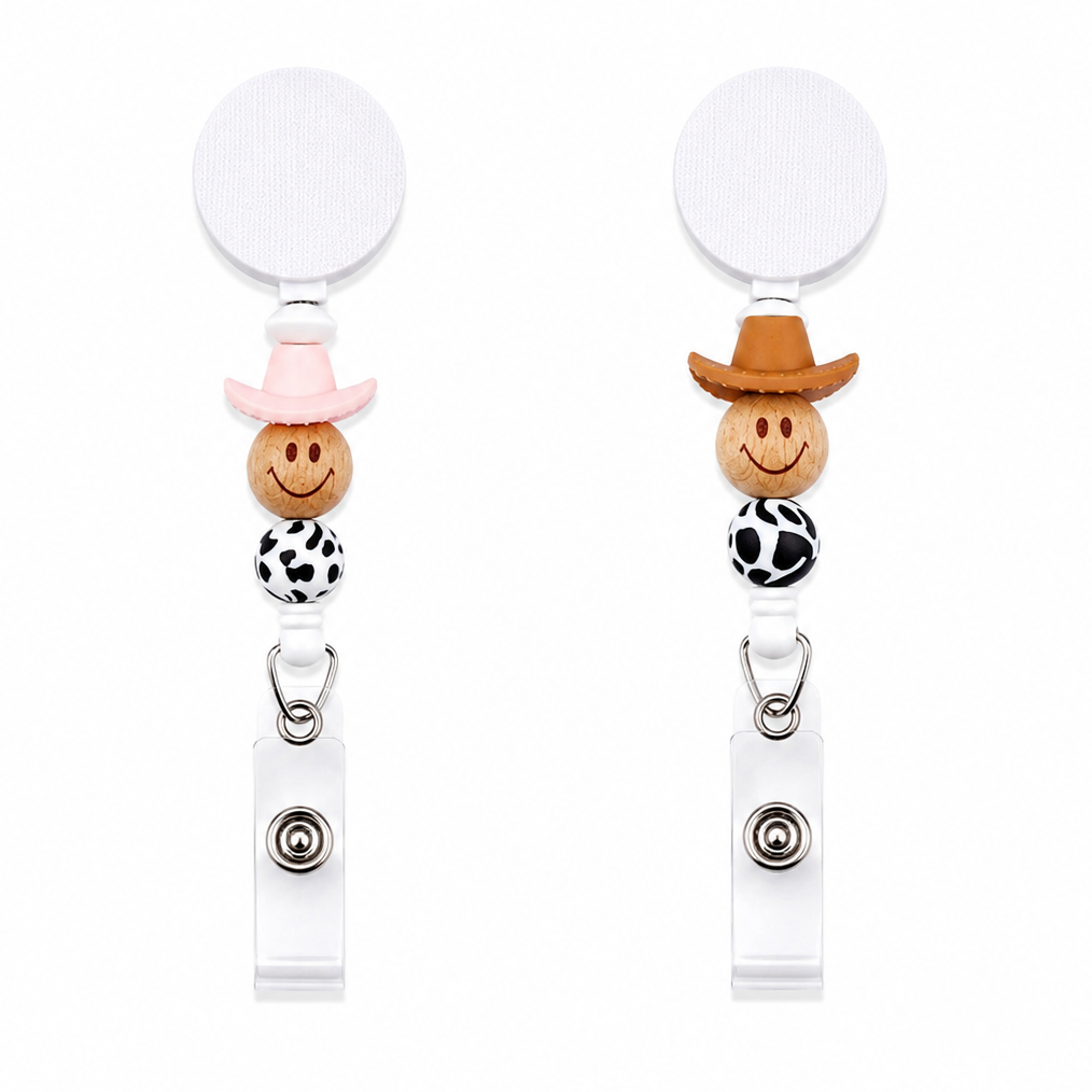 Western beaded badge reel featuring a smiling wooden face with pink cowgirl or brown cowboy hat, cow print silicone bead, white retractable badge reel, and badge holder.
