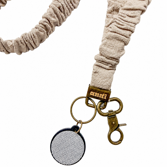 Linen Interchangeable Andi Lanyard featuring a soft neutral beige textured fabric design, compatible with interchangeable hardboards and plastic add-ons.