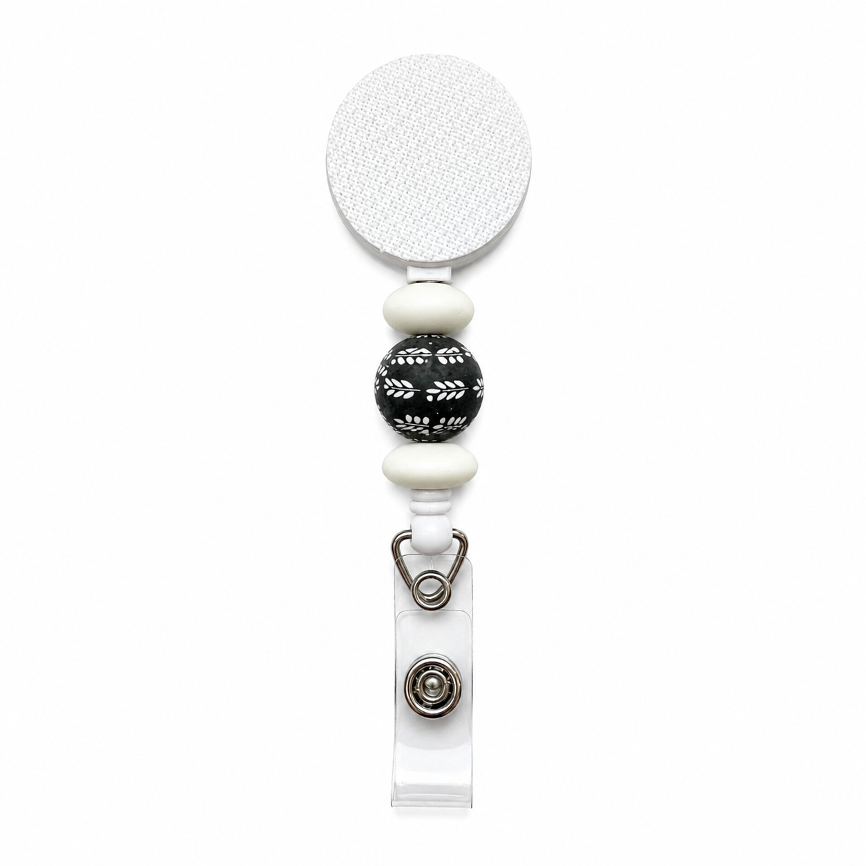 Midnight Laurel beaded badge reel featuring a black bead with white botanical leaves, white silicone accents, retractable reel, and clear badge holder attachment.