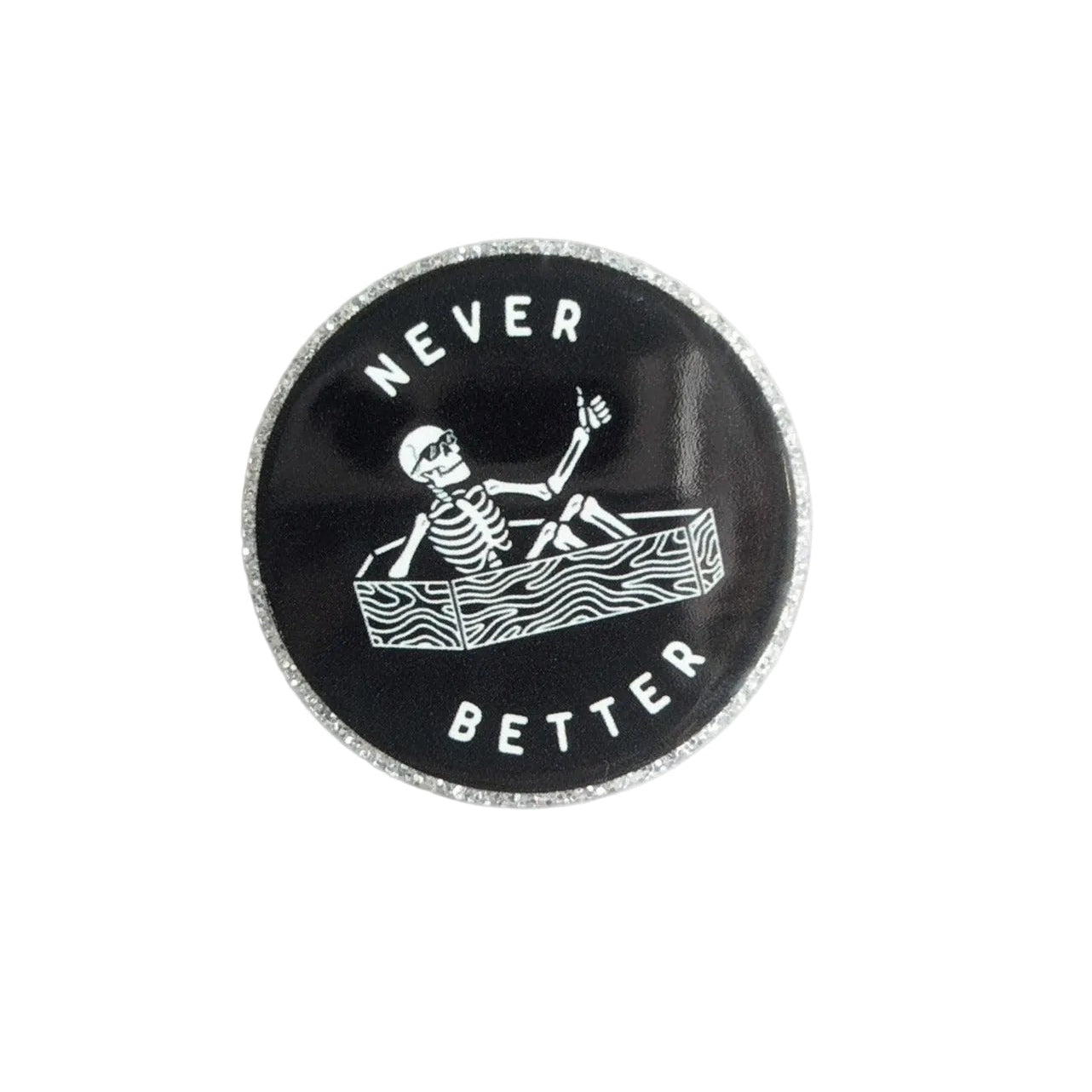 NEVER BETTER plastic add-on featuring a skeleton relaxing in a coffin on a black background, compatible with interchangeable badge reel bases, funny spooky accessory