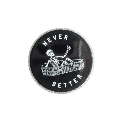 NEVER BETTER plastic add-on featuring a skeleton relaxing in a coffin on a black background, compatible with interchangeable badge reel bases, funny spooky accessory