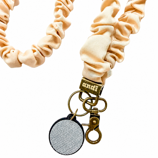 Oat Milk Interchangeable Andi Lanyard featuring a soft cream beige scrunchie-style fabric design, compatible with interchangeable hardboards and plastic add-ons.