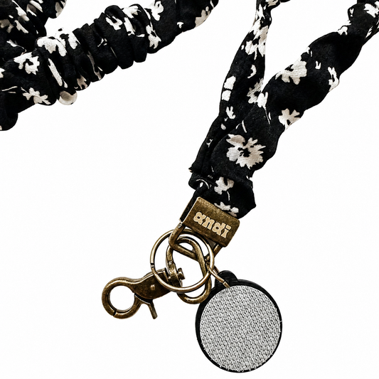 Onyx Floral Interchangeable Andi Lanyard featuring a black fabric scrunchie-style design with white floral print, compatible with interchangeable hardboards and plastic add-ons for personalized badge styling.