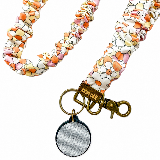 Peace and Love Interchangeable Andi Lanyard featuring a colorful floral fabric design with smiling flower accents, compatible with interchangeable hardboards and plastic add-ons.