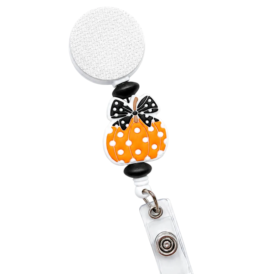 Polka Dot Bow Pumpkin badge reel featuring an orange pumpkin with white polka dots, a black-and-white polka dot bow, black decorative beads, a retractable badge reel, and secure badge holder attachment.