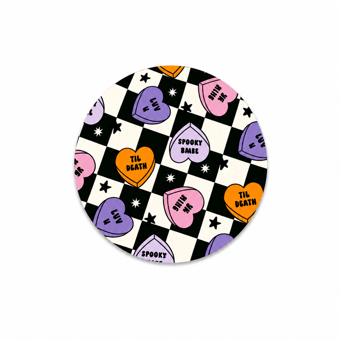 Hard board add-on featuring spooky conversation heart candies with "Spooky Babe," "Luv U," and "'Til Death" on a checkerboard background, compatible with interchangeable badge reel bases.