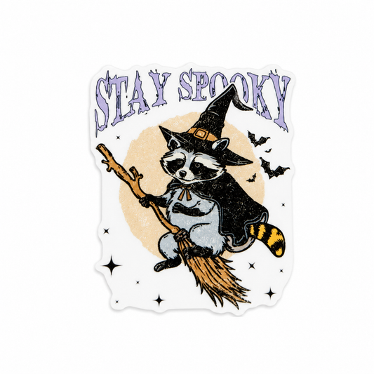 Plastic add-on featuring a raccoon dressed as a witch riding a broomstick with the text "STAY SPOOKY," compatible with interchangeable badge reel bases and perfect for Halloween lovers.