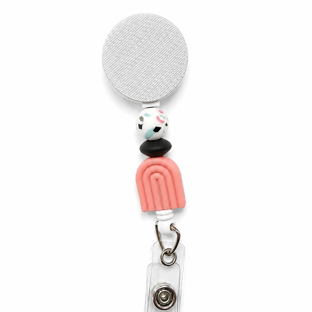 Terrazzo Rainbow badge reel featuring a pink rainbow focal bead, white terrazzo-pattern accent bead, black spacer bead, and a white retractable badge reel. Modern boho work badge accessory.