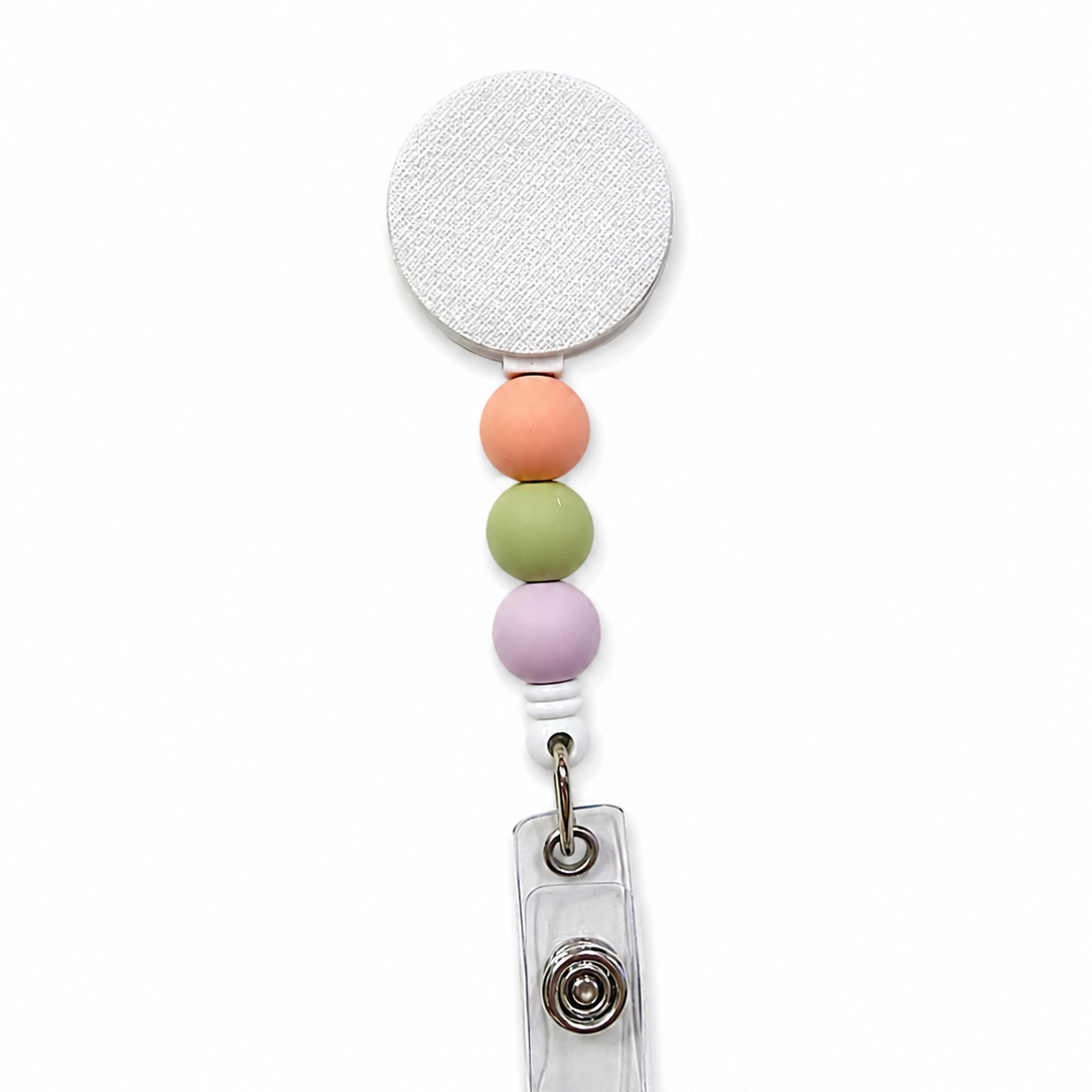 Wildflower fields badge reel featuring soft peach, sage green, and lavender decorative beads on a white retractable badge reel. Minimalist pastel beaded work badge accessory.